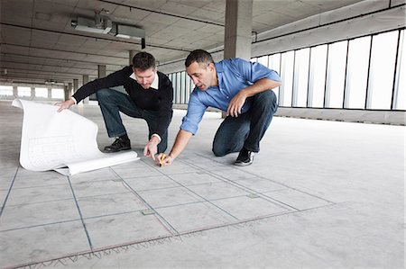 picture of people working - An architect and a business owner crouching over architectural plans and drawing on a concrete floor, planning a new office space in an empty raw built space. Stock Photo - Premium Royalty-Free, Code: 6118-09166268