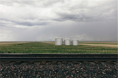 saskatchewan silo photos - Grain silos and storm clouds over vast farmland and prairie, train tracks in foreground Foto de stock - Sin royalties Premium, Código: 6118-09173761