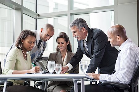 A mixed race group of male and female business people in a meeting at a conference table next to a large window in a convention centre. Stock Photo - Premium Royalty-Free, Code: 6118-09174095