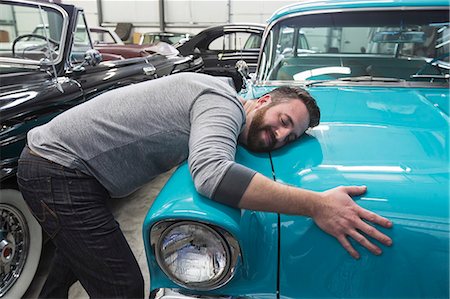 A Caucasian male hugging the hood of his old sedan in a classic car repair shop. Stock Photo - Premium Royalty-Free, Code: 6118-09174029