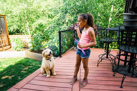 Tween Girl Blowing Bubbles with Labradoodle Puppy in Backyard Stock Photo - Premium Royalty-Free, Code: 6118-09183238