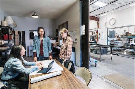 simsearch:6118-08660009,k - Three women gathered around table in office area of a metal workshop. Stock Photo - Premium Royalty-Free, Code: 6118-09112053
