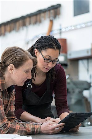 Two women standing at workbench in metal workshop, looking at digital tablet. Foto de stock - Sin royalties Premium, Código: 6118-09112006