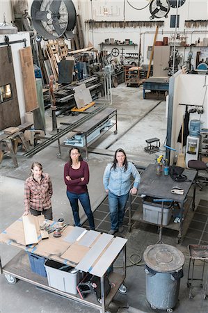 simsearch:6118-08660009,k - High angle view of three women standing in metal workshop, looking at camera. Stock Photo - Premium Royalty-Free, Code: 6118-09112027