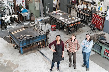 simsearch:6118-08660009,k - High angle view of three women standing in metal workshop, looking at camera. Stock Photo - Premium Royalty-Free, Code: 6118-09112030