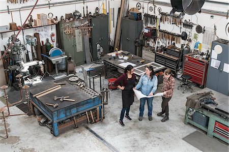 simsearch:6118-08660009,k - High angle view of three women standing in metal workshop, holding technical blueprint. Stock Photo - Premium Royalty-Free, Code: 6118-09112031