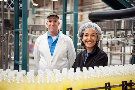 Portrait of a Caucasian male and African American female team of workers wearing head nets and standing near a conveyor belt of lemon flavoured water in a bottling plant. Stock Photo - Premium Royalty-Free, Code: 6118-09129408