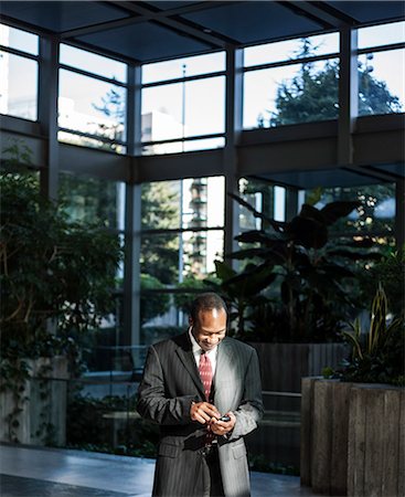simsearch:700-03058963,k - Black business man texting in a large lobby waiting area. Stock Photo - Premium Royalty-Free, Code: 6118-09129731