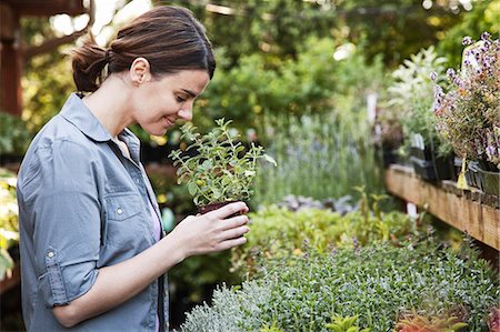 simsearch:6118-08660009,k - Caucasian woman holding a small plant, an aromatic herb and smelling it, shopping at a garden centre nursery. Stock Photo - Premium Royalty-Free, Code: 6118-09129801