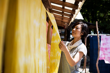 Japanese woman standing in a textile plant dye workshop, hanging up freshly dyed bright yellow fabric. Stock Photo - Premium Royalty-Free, Code: 6118-09200454