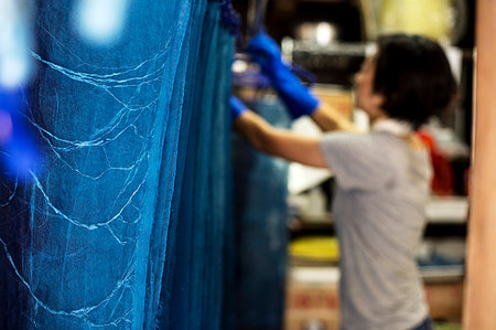 Japanese woman standing in a textile plant dye workshop, hanging up freshly dyed bright blue fabric. Stock Photo - Premium Royalty-Free, Code: 6118-09200459