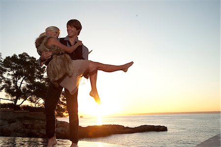 Man carrying girlfriend by the ocean at sunset Stock Photo - Premium Royalty-Free, Code: 6122-07696784