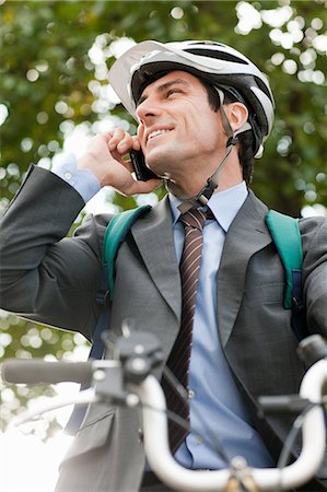 Mid adult businessman using cellphone on bicycle Stock Photo - Premium Royalty-Free, Code: 6122-07697784