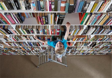 Boy using stepladder on bookshelves Stock Photo - Premium Royalty-Free, Code: 6122-07699008