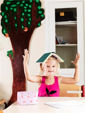 Girl balancing book on head at desk Stock Photo - Premium Royalty-Free, Code: 6122-07702288