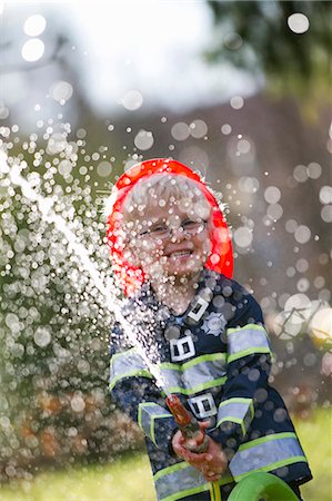 Boy in fireman costume playing with hose Stock Photo - Premium Royalty-Free, Code: 6122-07703637