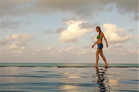 Woman walking at edge of infinity pool Stock Photo - Premium Royalty-Free, Code: 6122-07707464