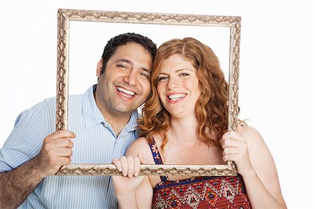 frames - Couple smiling throrugh picture frame against white background Stock Photo - Premium Royalty-Free, Code: 6122-08212572