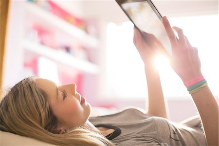 Teenage girl using digital tablet in sunny bedroom Stock Photo - Premium Royalty-Free, Code: 6124-08170472