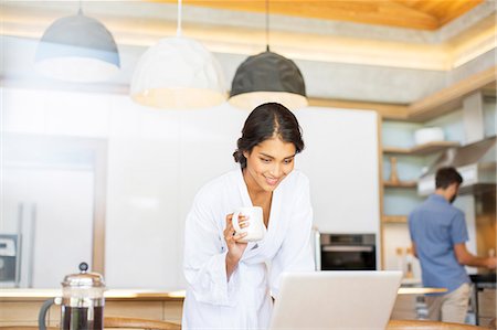 robe - Woman in bathrobe drinking coffee and using laptop in kitchen Stock Photo - Premium Royalty-Free, Code: 6124-08170642