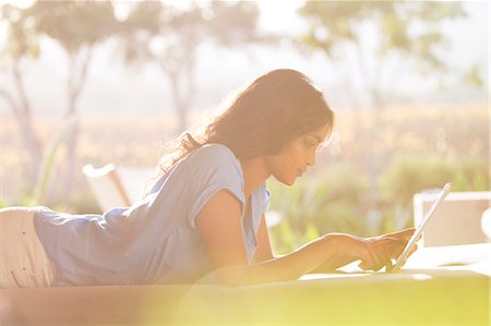 Woman laying using digital tablet on sunny patio Stock Photo - Premium Royalty-Free, Code: 6124-08170628