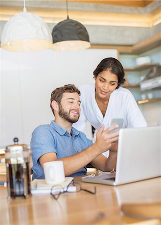 Couple texting with cell phone at laptop Stock Photo - Premium Royalty-Free, Code: 6124-08170638