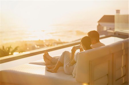 Silhouette couple using cell phone on chaise lounge with sunset ocean view Stock Photo - Premium Royalty-Free, Code: 6124-08743314