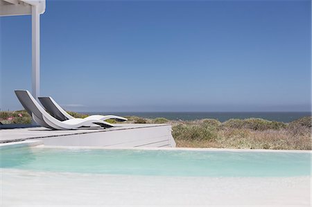 simsearch:6113-07147822,k - Swimming pool and modern lounge chairs overlooking ocean view under sunny blue sky Photographie de stock - Premium Libres de Droits, Code: 6124-08703854