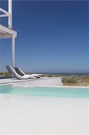 simsearch:6113-07147822,k - Modern lounge chairs at poolside with ocean view under sunny blue sky Photographie de stock - Premium Libres de Droits, Code: 6124-08703869