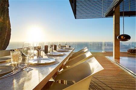 simsearch:6124-08703974,k - Sun shining over ocean behind luxury patio dining table with placesettings Stock Photo - Premium Royalty-Free, Code: 6124-08703989