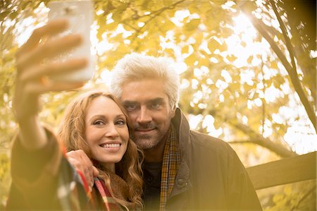 simsearch:6108-06166561,k - Smiling couple taking selfie with camera phone under autumn tree Foto de stock - Sin royalties Premium, Código: 6124-08820771