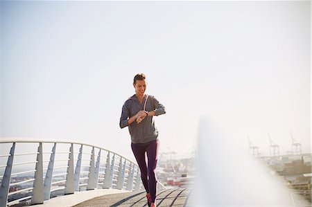 sweatshirt - Smiling female runner checking smart watch fitness tracker on sunny urban footbridge Stock Photo - Premium Royalty-Free, Code: 6124-08820808