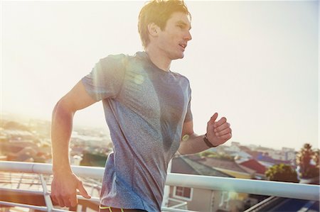 Sweaty male runner running on sunny urban footbridge at sunrise Stock Photo - Premium Royalty-Free, Code: 6124-08820839