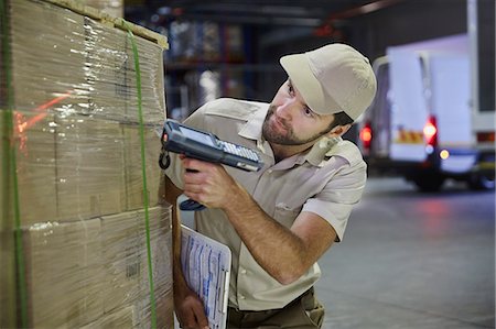 Truck driver worker with scanner scanning pallet of boxes in distribution warehouse Stock Photo - Premium Royalty-Free, Code: 6124-08820983
