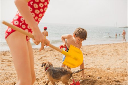 Boy and girl brother and sister playing with dog and digging in sand with shovels on sunny beach Stock Photo - Premium Royalty-Free, Code: 6124-08945986