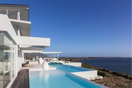 simsearch:6113-07147822,k - Sunny, tranquil modern luxury home showcase exterior with infinity pool and ocean view under blue sky Photographie de stock - Premium Libres de Droits, Code: 6124-08908210