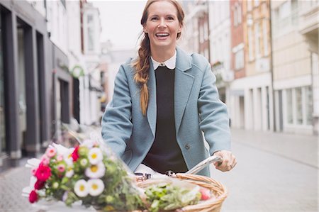 person in a basket of a bike - Smiling woman riding bicycle with flowers in basket Stock Photo - Premium Royalty-Free, Code: 6124-08926768