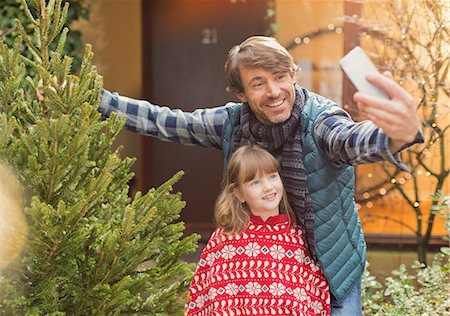 Father and daughter taking selfie with Christmas tree outside of house Stock Photo - Premium Royalty-Free, Code: 6124-08926886