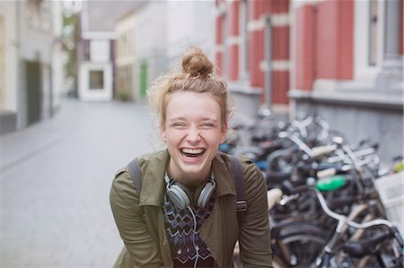 Portrait enthusiastic, laughing young woman with headphones on city street Stock Photo - Premium Royalty-Free, Code: 6124-08926830