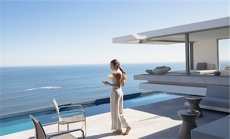 simsearch:6113-07790529,k - Woman walking and texting with smart phone on sunny modern, luxury home showcase patio with ocean view Stock Photo - Premium Royalty-Free, Code: 6124-09099768
