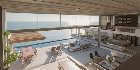 simsearch:6124-08703974,k - Elevated view modern, luxury home showcase interior living room and patio with sunny ocean view Stock Photo - Premium Royalty-Free, Code: 6124-09099810