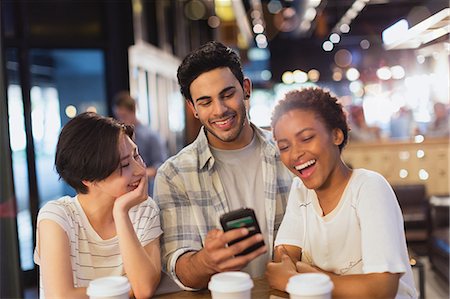 simsearch:6113-08743448,k - Young friends using cell phone, texting and laughing at cafe Stock Photo - Premium Royalty-Free, Code: 6124-09004795