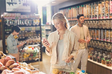 Young woman using cell phone, grocery shopping in market Stock Photo - Premium Royalty-Free, Code: 6124-09004841