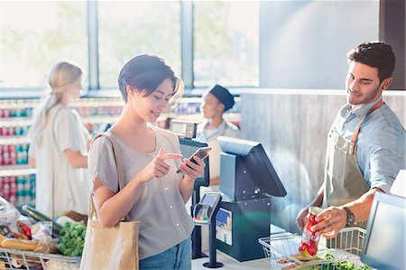 store counter working - Young woman using cell phone at grocery store market checkout Stock Photo - Premium Royalty-Free, Code: 6124-09004866