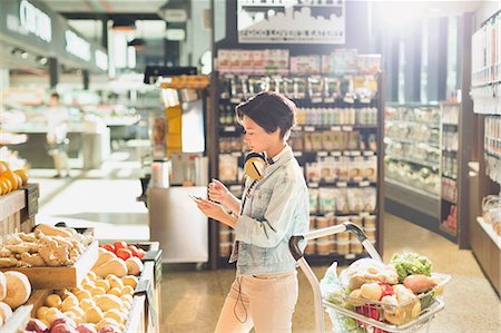 simsearch:700-01163575,k - Young woman with headphones using cell phone, grocery shopping in market Stock Photo - Premium Royalty-Free, Code: 6124-09004878