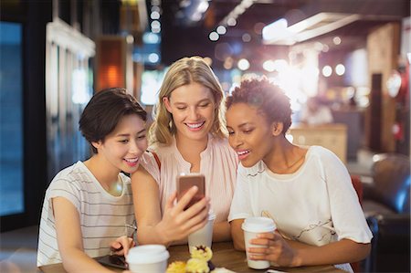 simsearch:6113-08743448,k - Young women friends using cell phone and drinking coffee in cafe Stock Photo - Premium Royalty-Free, Code: 6124-09004816