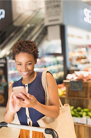 simsearch:700-01163575,k - Smiling young woman using cell phone in grocery store market Stock Photo - Premium Royalty-Free, Code: 6124-09004832