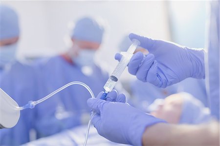 surgical gown - Close up anesthesiologist with syringe injecting anesthesia medicine into IV drip in operating room Stock Photo - Premium Royalty-Free, Code: 6124-09026385