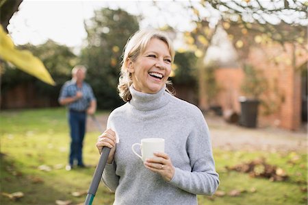 raking leaves autumn - Happy mature woman drinking coffee and raking autumn leaves in backyard Stock Photo - Premium Royalty-Free, Code: 6124-09167213