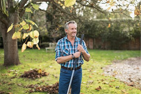 raking leaves autumn - Smiling senior man raking autumn leaves in backyard Stock Photo - Premium Royalty-Free, Code: 6124-09167228